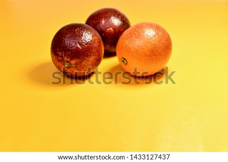 3 red oranges in the center from above on a yellow substrate. Located close to each other. Glossy shiny skin.