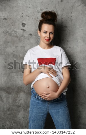 Beautiful young pregnant happy mother woman in white t-shirt posing on dark background