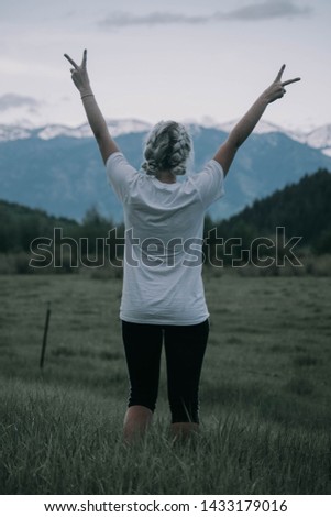 A young adventurer exploring Idaho for the first time. She throws up a peace sign in front of the scenic mountain tops. 