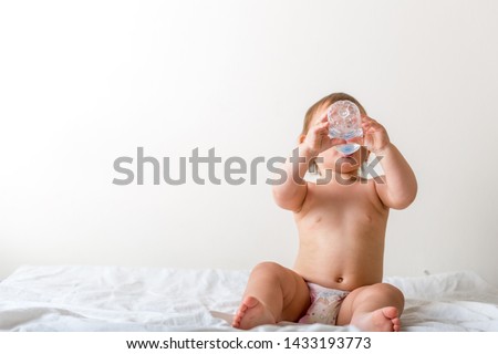 Toddler baby drink water from blue plastic bottle. Sitting on white background. Copy space