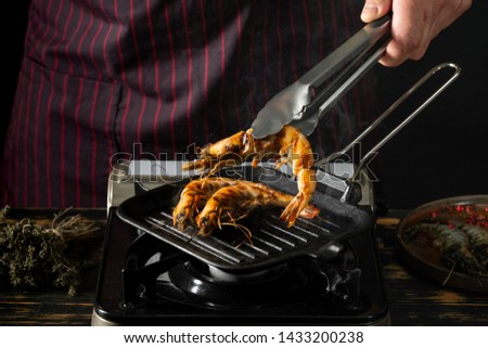 Seafood shrimps cooking by chef hands on grill pan on kitchen background copy space. Cooking food concept.