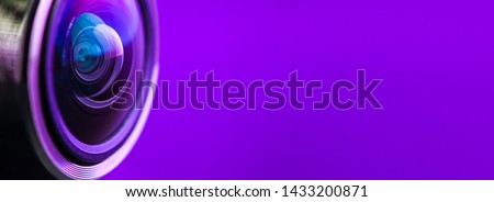  Camera lens and dark purple backlight. Side view of the lens of camera on purple background. Camera Lens Close Up. Optics. Banner.