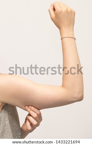 A close up view of a Caucasian woman squeezing her arm showing saggy muscles and skin in her upper arm, commonly referred to as bingo wings. Isolated with copy space above the arm. Royalty-Free Stock Photo #1433221694
