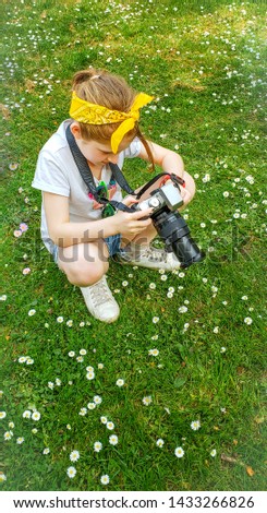Cute girl takes photos of small white flowers with SLR camera  in park in summer