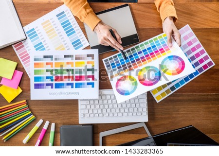 Image of female creative graphic designer working on color selection and drawing on graphics tablet at workplace with work tools and accessories, top view workspace.