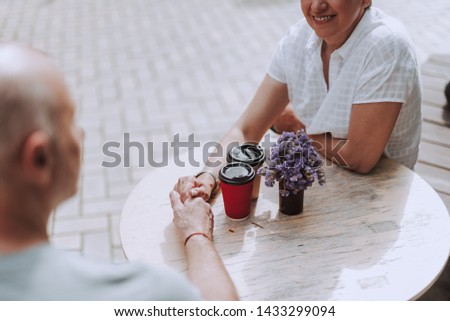 Cropped photo of happy gray-haired male and female sitting in cafe and drinking coffee while looking each other