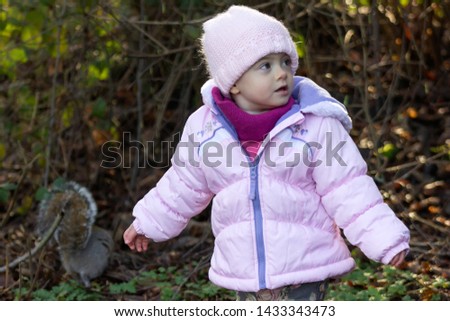 20 months old baby enjoying the nice weather outside. Toddler girl portraits in natural light. Little girl close up picture in nature, in Winter. pointing out a squirrel 