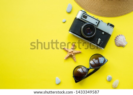 Summer accessories concept on yellow background, flatlay, copyspace, vintage camera, white sunglasses and swimsuit.