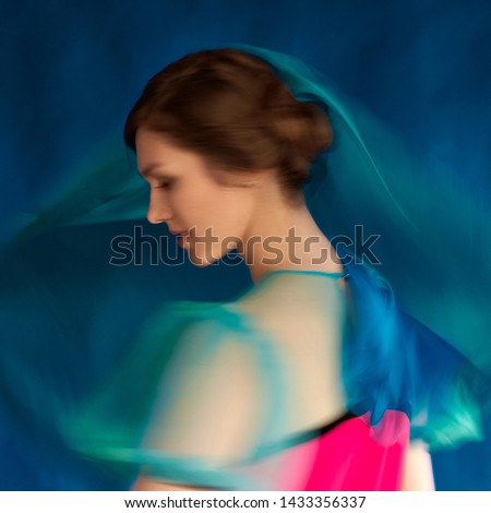 Girl dancing contemporary with blue fabric indoors on blue background. Blurred artsy fashion style picture in motion that shows the moment of moving.