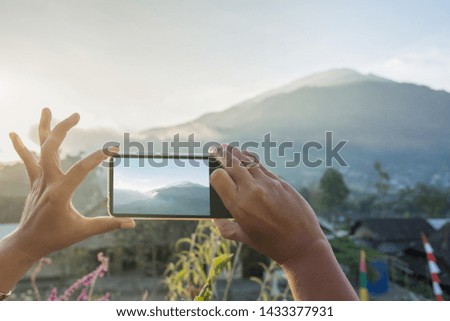 Womans hand taking photo of mouintain in late afternoon with phone.