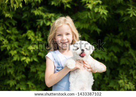 Little girl holding white puppy in her arms.