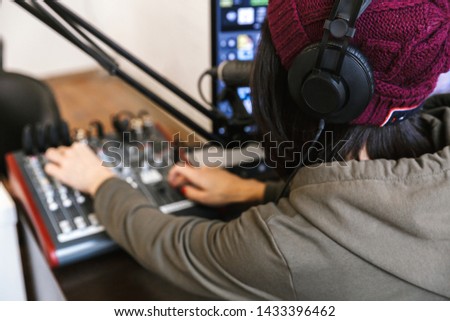 Close up of a young female radio host broadcasting in studio, using computer and headphones