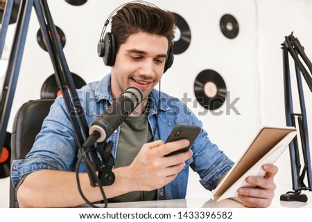 Handsome happy young male radio host broadcasting in studio, using microphone and headphones
