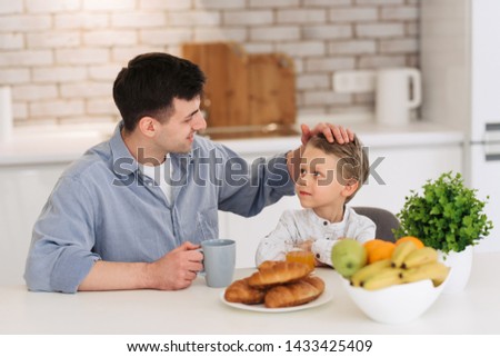 Father and son are talking and smiling while having a breakfast on kitchen.