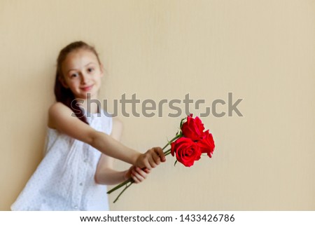 Small charming schoolgirl pereds bouquet of red flowers. Isolated on beige background.