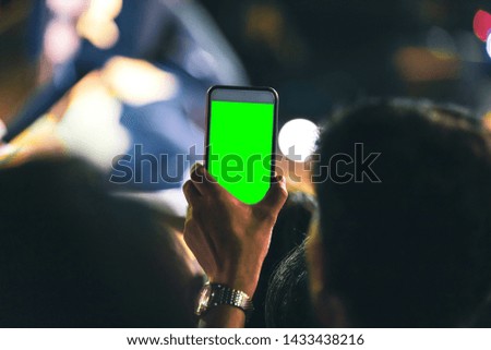 Hands of people holding mobile smart phone with green screen recording and taking a picture at music concert
