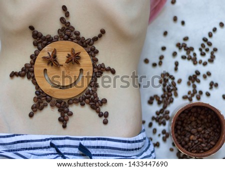 Coffee is a healthy, mood-enhancing drink. Star sun with a smile of coffee beans on the belly of a young girl. No face.