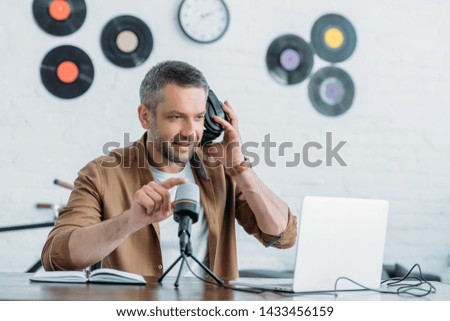 handsome radio host holding adjusting headphones and microphone in broadcasting studio