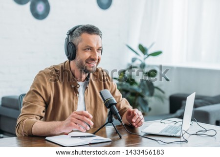 smiling radio host in headphones recording podcast in broadcasting studio