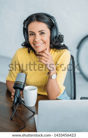 pretty radio host in headphones smiling at camera while sitting near microphone