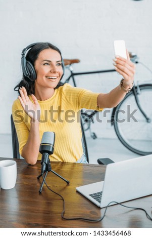 cheerful radio host waving hand while having video chat in smartphone
