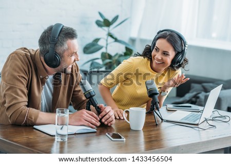 two radio hosts in headphones laughing while recording podcast in studio together Royalty-Free Stock Photo #1433456504