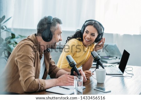 two smiling radio hosts talking while recording podcast in studio together