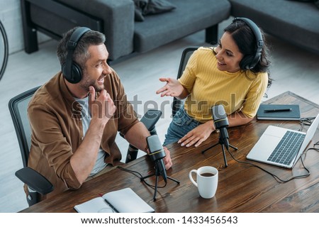 two radio hosts talking and smiling while sitting near microphones in broadcasting studio