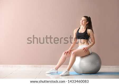 Young sporty woman with fitball near color wall