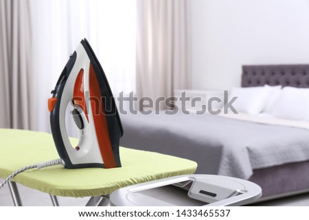 Modern electric iron on board in bedroom, space for text. Laundry day