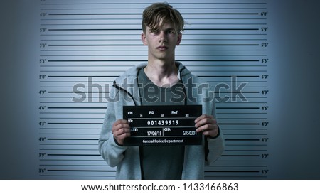 In a Police Station Arrested Drug Addict Teenage Posing for a Front View Mugshot. He is Heavily Bruised. Height Chart in the Background. Royalty-Free Stock Photo #1433466863
