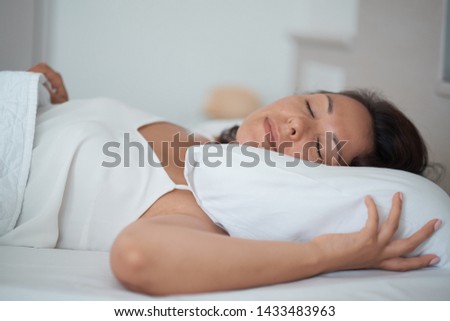 Closed up image of an Asian woman sleeping in a bed with a light smile on her face, flare lighting from the window.