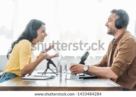 two smiling radio hosts talking while recording podcast in broadcasting studio
