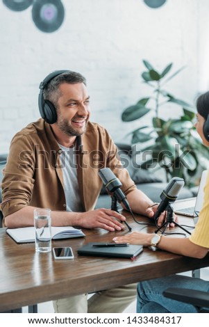 cheerful radio hosts in headphones recording podcast in broadcasting studio
