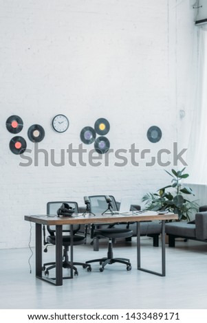 spacious, furnished radio studio with wooden desk, office chairs and vinyl discs on white wall
