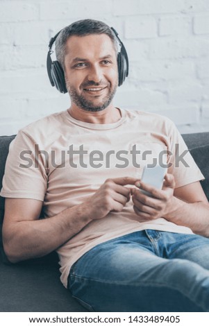 cheerful man in headphones using smartphone while looking away