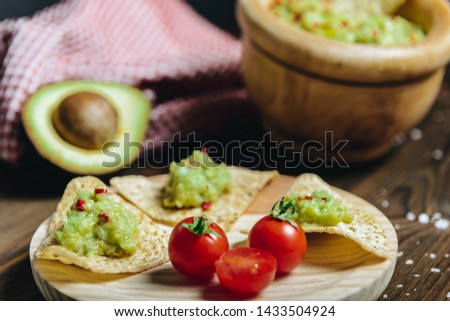 nachos with homemade guacamole in a wood plate next to an avocado and a kitchen rag, typical mexican healthy vegan cuisine with rustic dark food photo style, selective focus