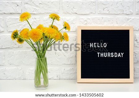 Hello Thursday words on black letter board and bouquet of yellow dandelions flowers on table against white brick wall. Concept Happy Thursday. Template for postcard. Royalty-Free Stock Photo #1433505602