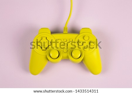 a yellow painted video game controller on a plain pink background. Minimal color still life photography