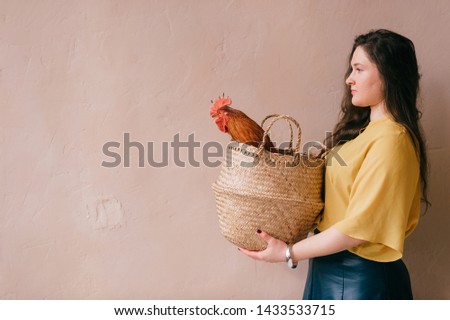 Young stylish girl holding basket with chicken on abstract background