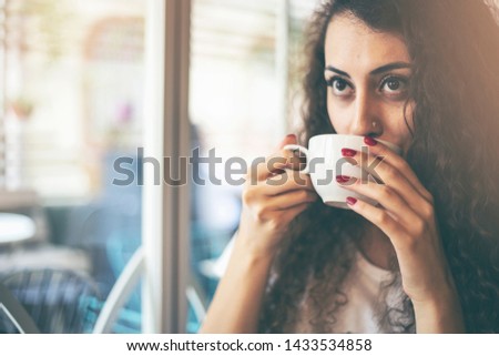 Beautiful smiling woman drinking coffee at cafe. Portrait of young woman in a cafeteria drinking hot cappuccino. Pretty woman with cup of coffee.