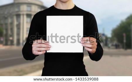 A man holding a white sheet of paper. Holding a booklet. Close up. The background of the city.