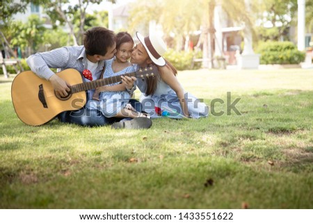 Happy Asian family. Father, mother and daughter  in kissing at a park at natural sunlight background. Family vacation concept.