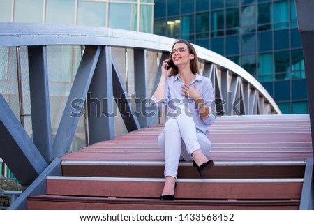 Happy smiling business woman talking on mobile smartphone in the street with office buildings in the background.