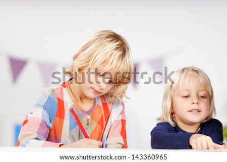 Two small young blonde caucasian sisters drawing pictures with color pencils