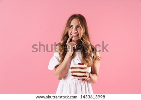 Image of happy thinking woman wearing white dress looking upward with her finger on her teethes and holding piece of cake isolated over pink background