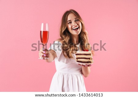 Image of nice smiling woman wearing white dress holding piece of cake and glass of wine isolated over pink background