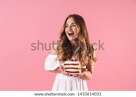 Image of happy smiling woman wearing white dress looking aside and holding piece of cake isolated over pink background