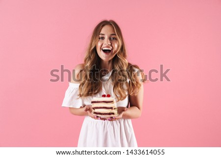 Image of happy surprised woman wearing white dress smiling at camera and holding piece of cake isolated over pink background