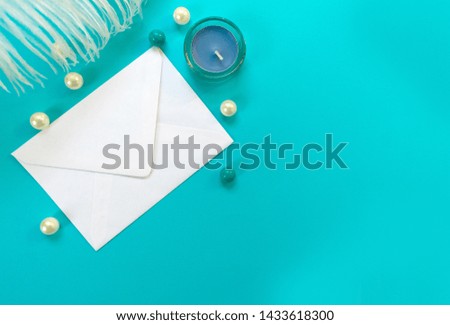White envelope white feather and blue candle isolated on blue background. Greeting card concept. Copy space.